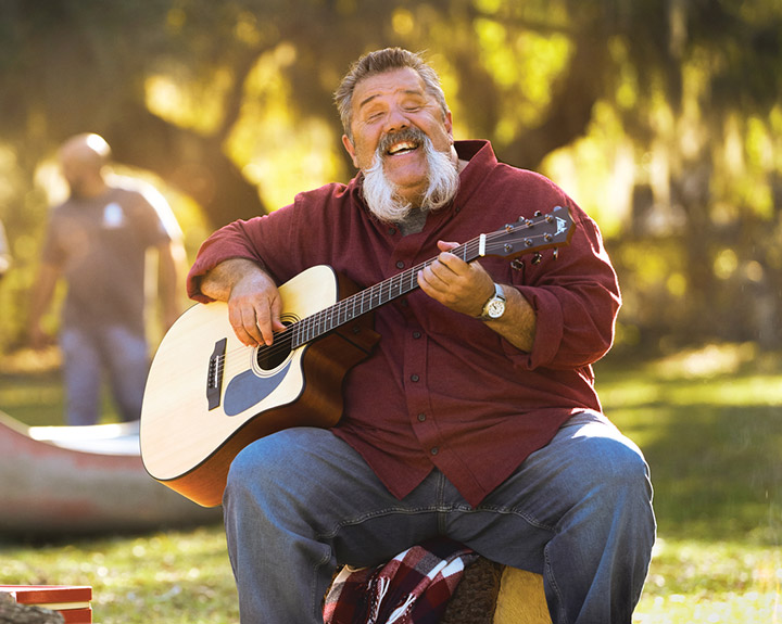 Wounded warrior Aaron Cornelius playing the guitar around a fire during an outdoor event.