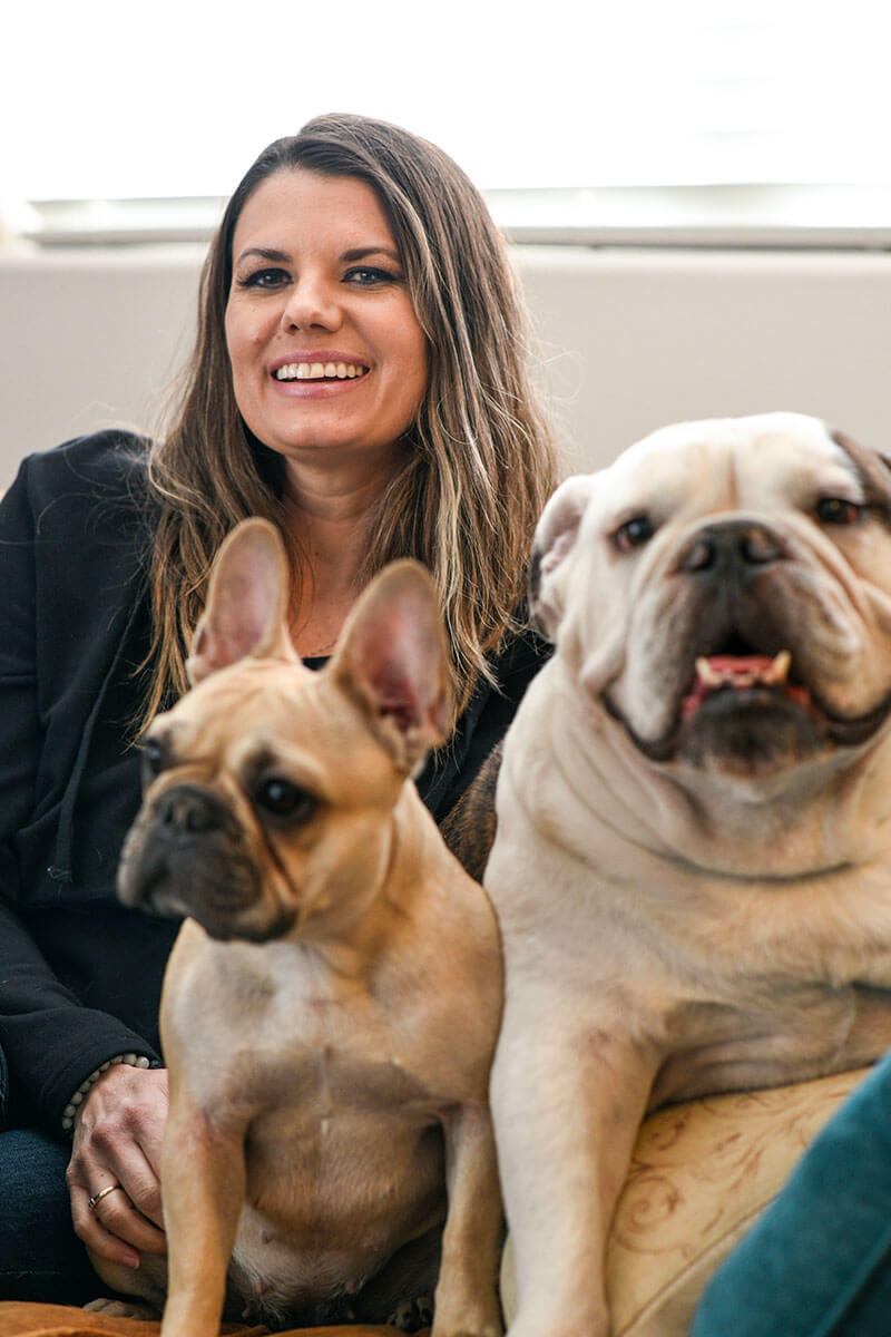 Wounded warrior Melissa McMahon sitting at home on a couch with her two dogs smiling.