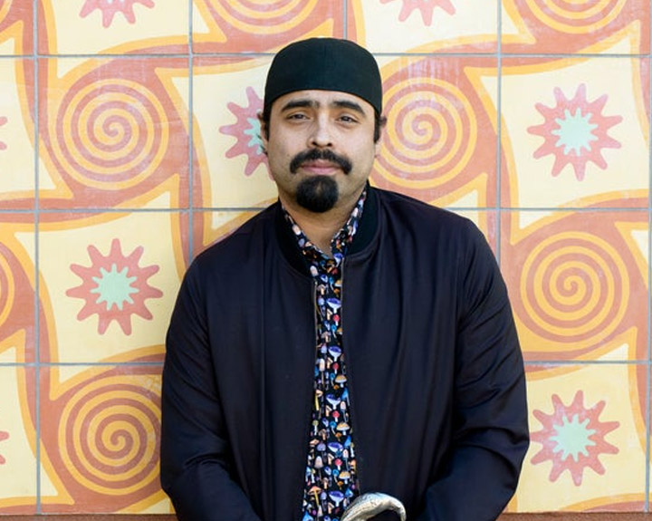 Sal Gonzalez stands smiling in front of a colorful tile wall.