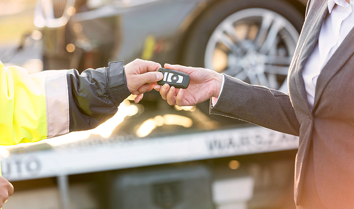 Tow truck driver giving car keys to business woman.